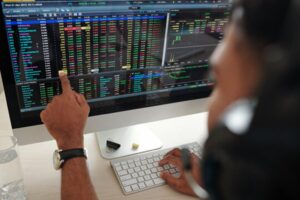 A image shows a person who is putting his finger on computer and showing the charts of share market which makes the clear difference between shares and stocks 